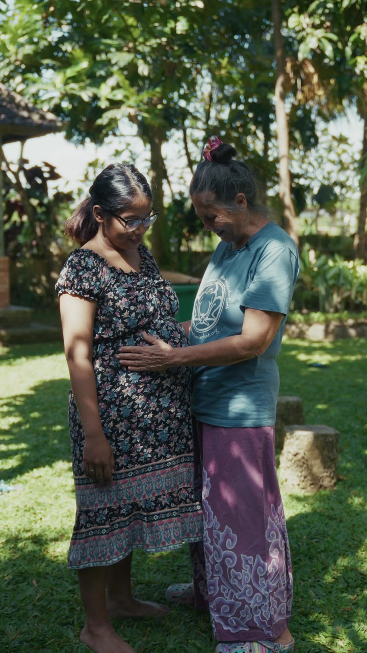Les mains d’une professionnelle de la naissance sur le ventre d’une femme enceinte, au jardin